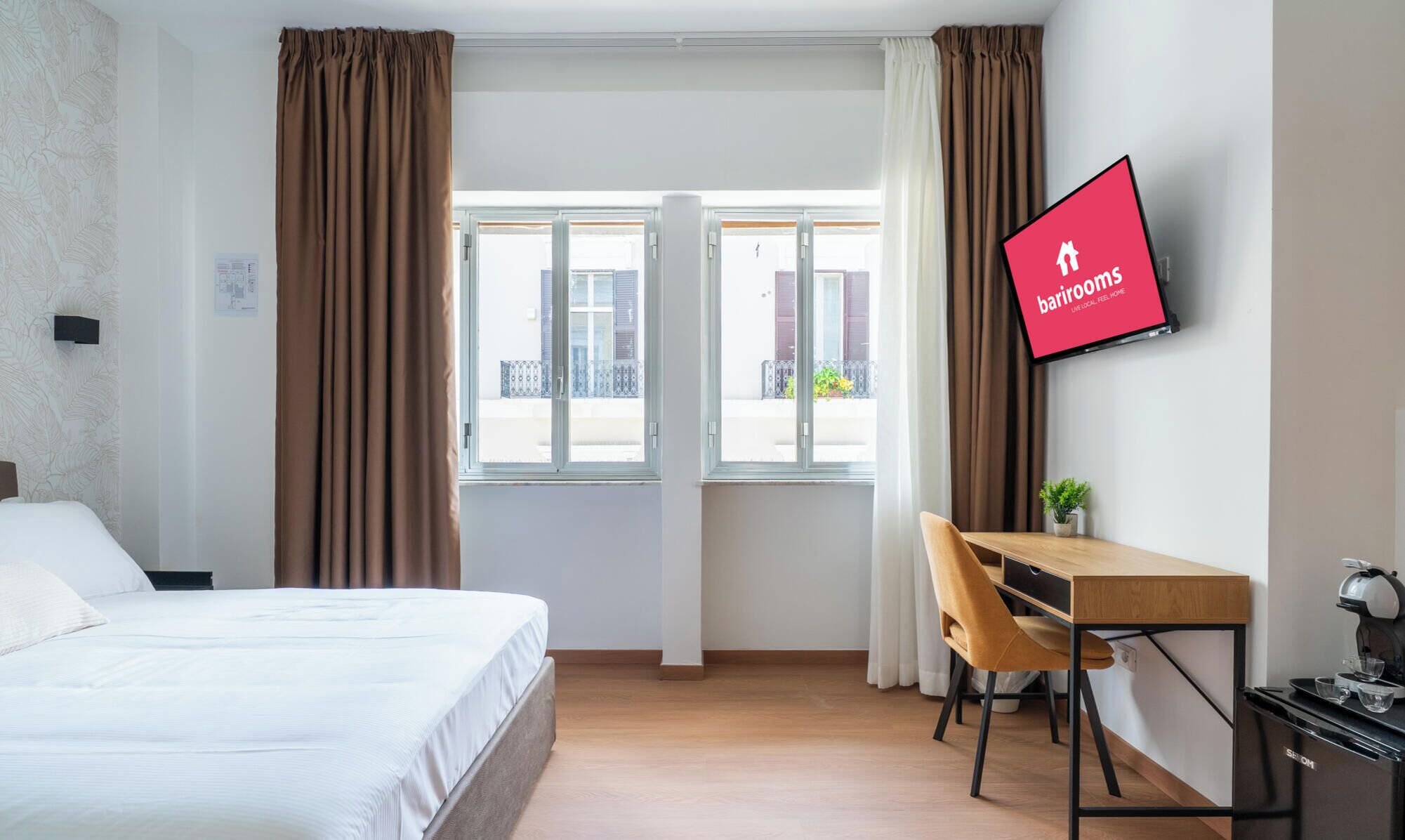 Habitación de hotel con cama, escritorio, silla, televisor y ventana con cortinas.