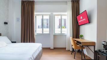 Habitación de hotel con cama, escritorio, silla, televisor y ventana con cortinas.