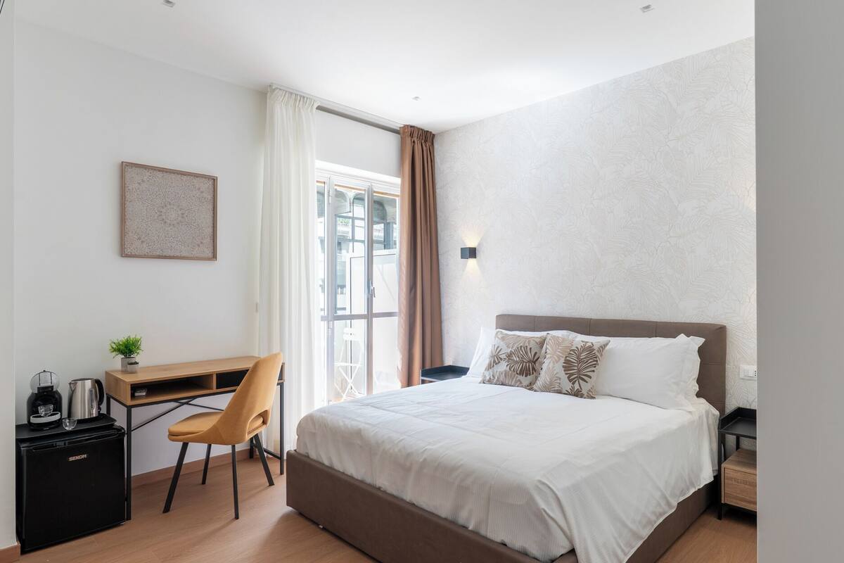 Un dormitorio con una cama, un escritorio, una silla, una cafetera y un refrigerador.
