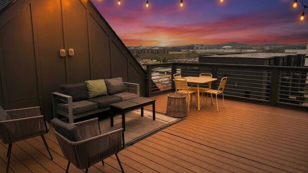 Une terrasse sur le toit, dotée d’un sol en bois, d’un canapé, de chaises, d’une table et de guirlandes lumineuses.