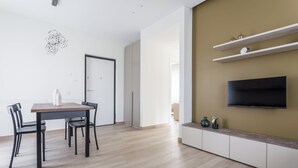 A modern living room with a flat-screen TV, wooden flooring, a dining area with a table and chairs, and built-in shelving with decorative items. - Residenze Vesuviane - Pompei (Terzigno)