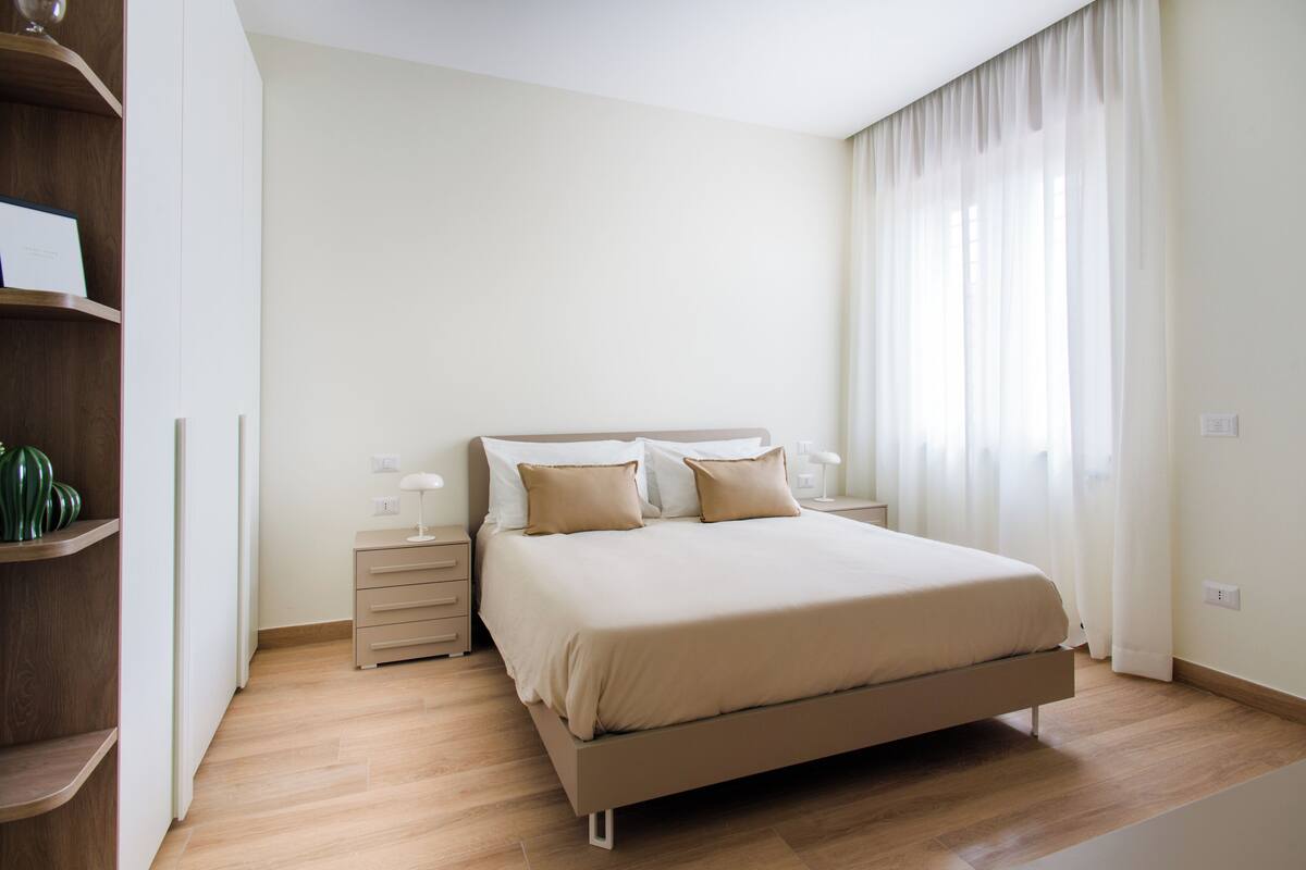 Een slaapkamer met een bed, nachtkastjes, een kledingkast en een raam met gordijnen.