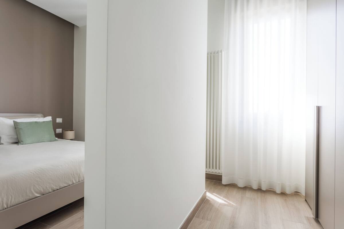 Een slaapkamer met een bed, nachtkastje, radiator en een raam met gordijnen.