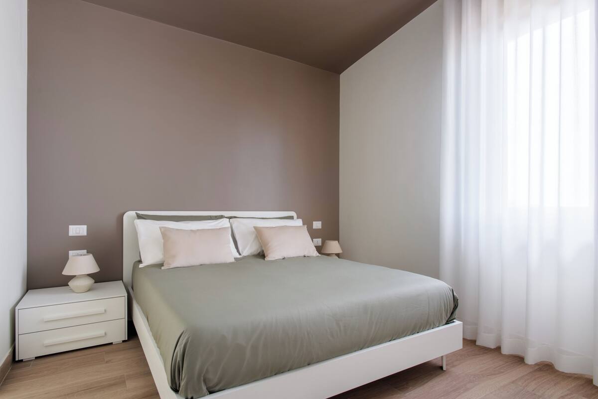 Een slaapkamer met een bed, nachtkastjes en een raam met gordijnen.