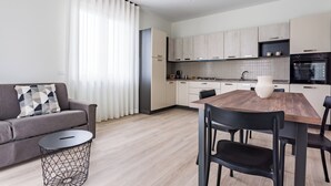 A modern kitchen with light wood cabinets, a dining table with chairs, a sofa, and a small round table with a geometric design. - Residenze Vesuviane - Pompei (Terzigno)