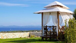 A gazebo with a white canopy, a stone wall, and a grassy area with a view of the sea and mountains. - Villa Carla (Bonifacio)