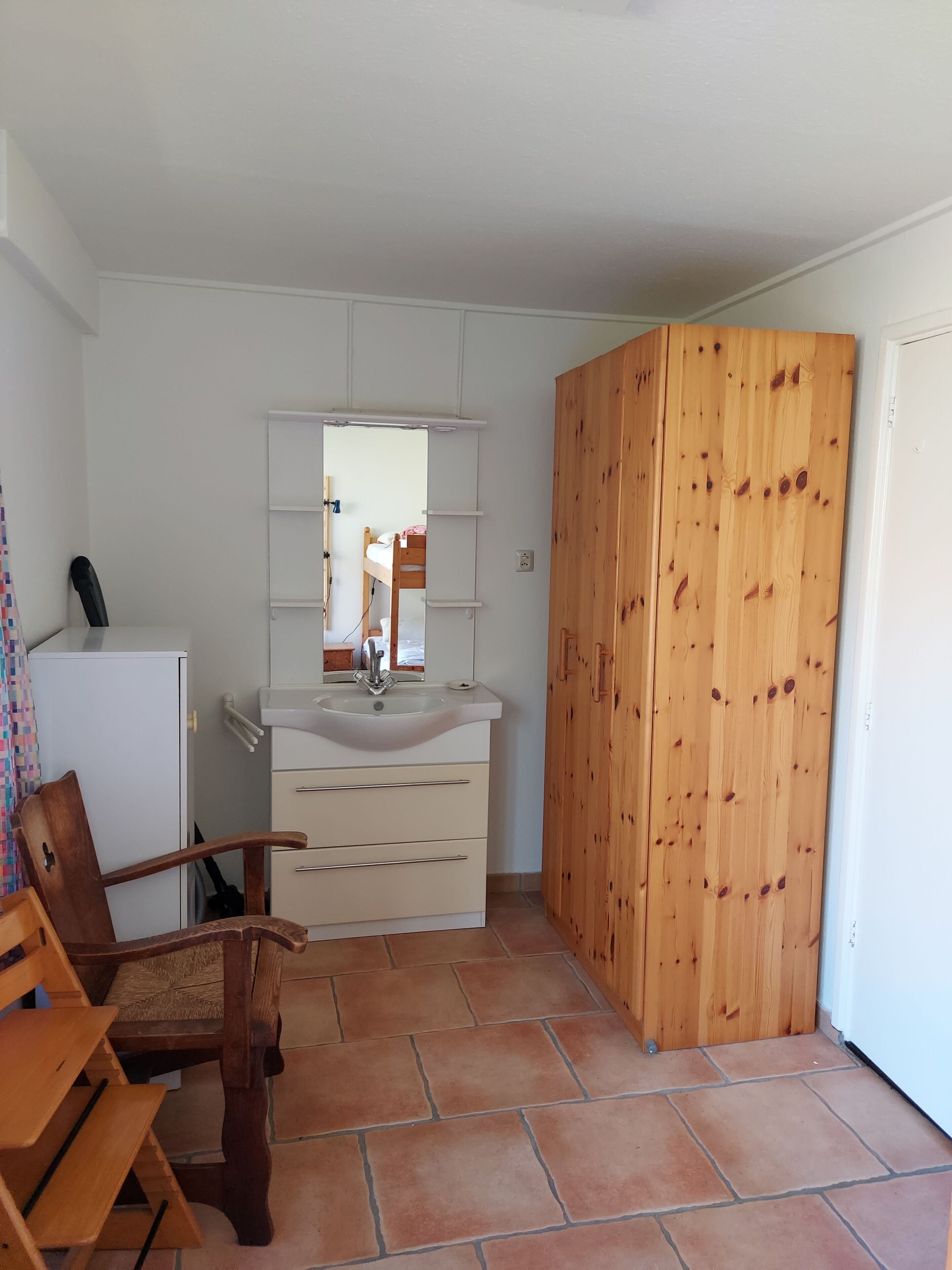 A compact room with a wooden wardrobe, a white sink, and a chair.