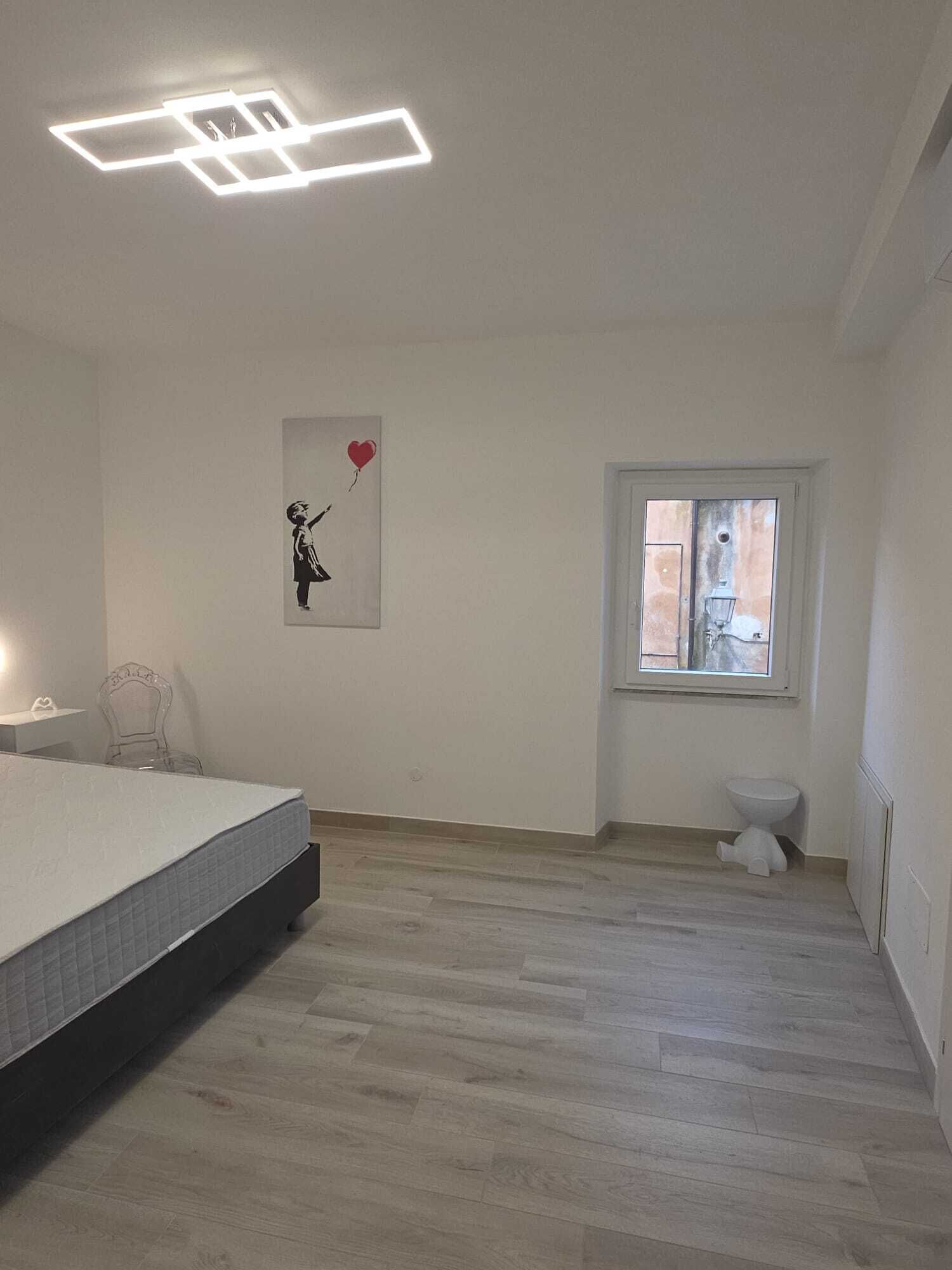 Een slaapkamer met een bed, een raam, een toilet en een wandlamp.