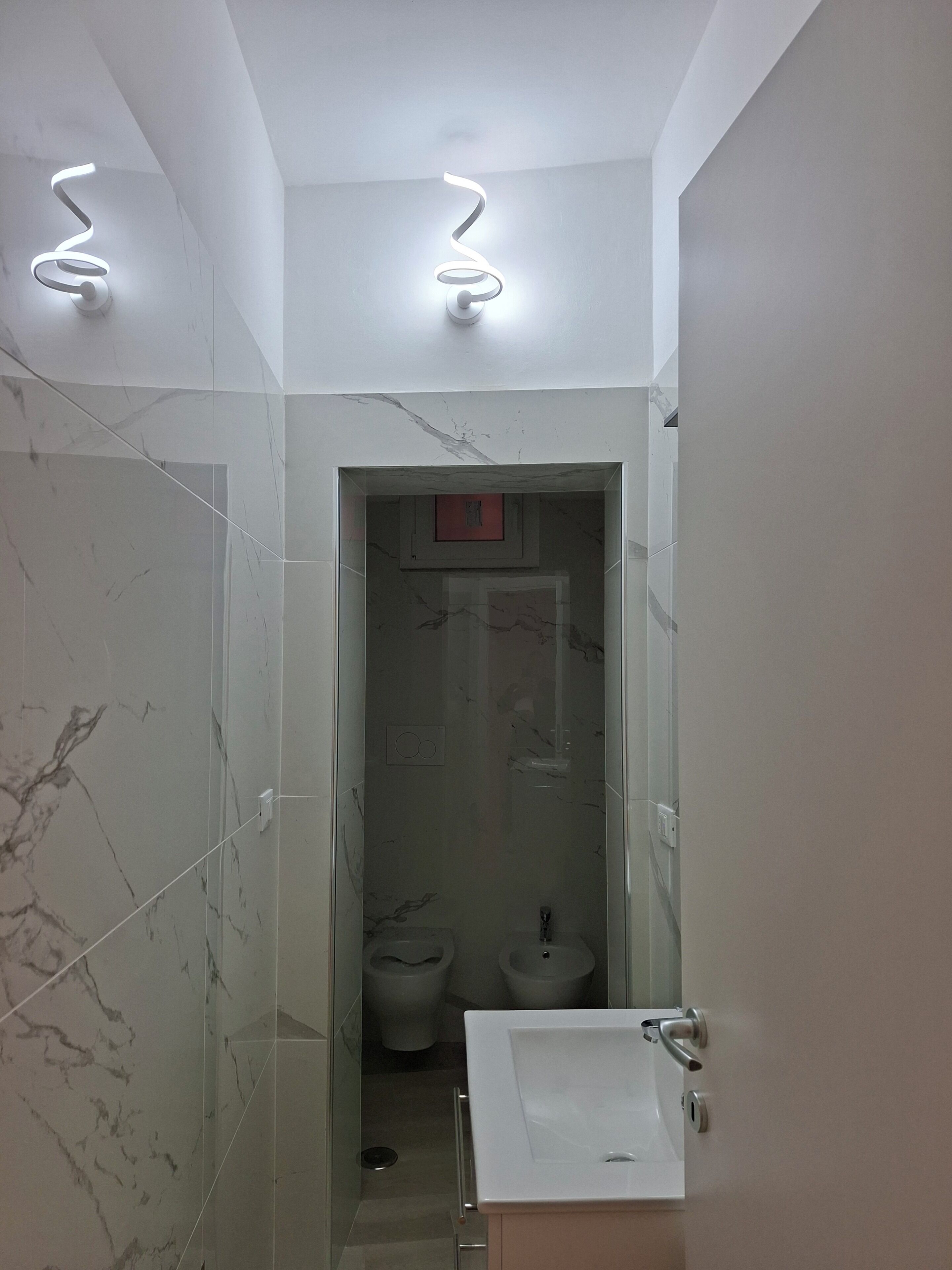 Ein Badezimmer mit Marmorwand, einem Waschbecken und zwei Toiletten.