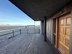 Une terrasse en bois offrant une vue sur un bâtiment aux toits rouges et sur des montagnes au loin.