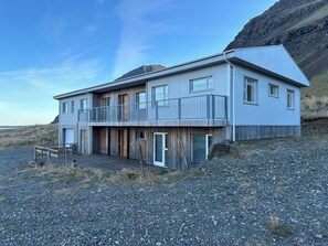 A two-story building with a balcony, wooden doors, and a view of the beach.