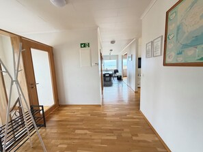 A hallway with wooden flooring, a metal rack, a door, and a view of a beach through a window.