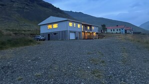 A two-story building with a gravel driveway, a car parked in front, and a mountain in the background.
