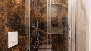 Un baño moderno con ducha de vidrio, paredes de mármol y un inodoro a la vista.