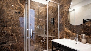 Un baño moderno con ducha de vidrio, un lavamanos blanco y pared de mármol.