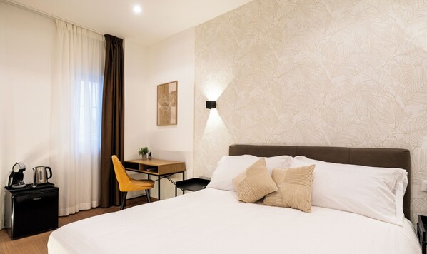 A hotel room with a bed, a desk, a chair, a coffee maker, and a wall-mounted light. - Opera Suites (Bari)