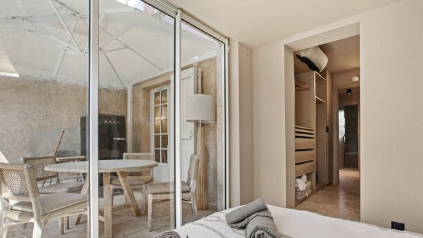 Una moderna camera d'albergo con parete in vetro, un letto con asciugamani arrotolati, un'area pranzo con tavolo e sedie, e un cabina armadio.