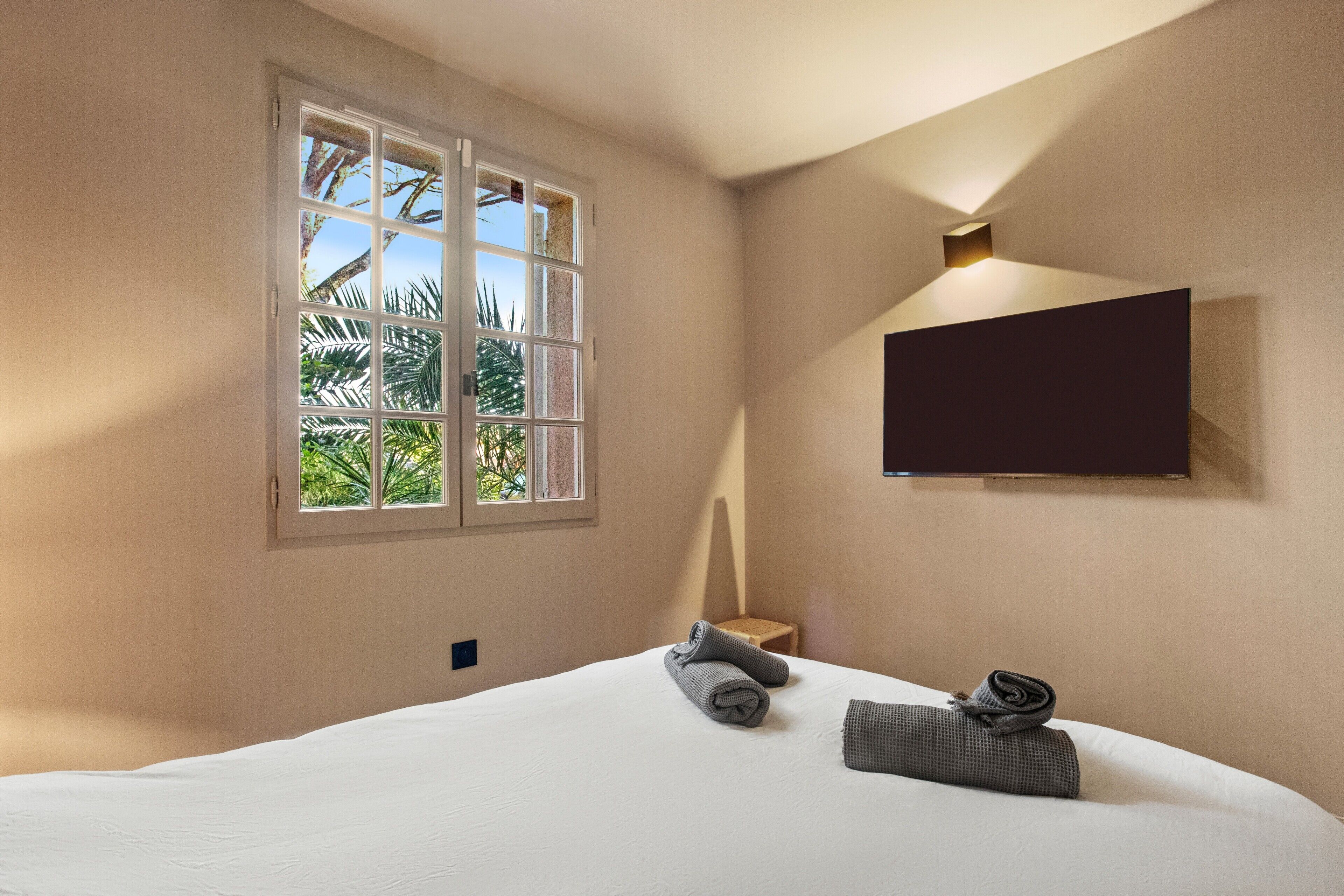 Une chambre avec un grand lit, une fenêtre donnant sur un paysage verdoyant, un téléviseur fixé au mur et une petite table avec des serviettes.