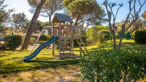 Un'area giochi con scivolo e angolo arrampicata, circondata da alberi e erba.