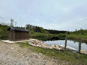 Eine Holzhütte an einem ruhigen See mit einem Steg, umgeben von Grün und Bäumen.