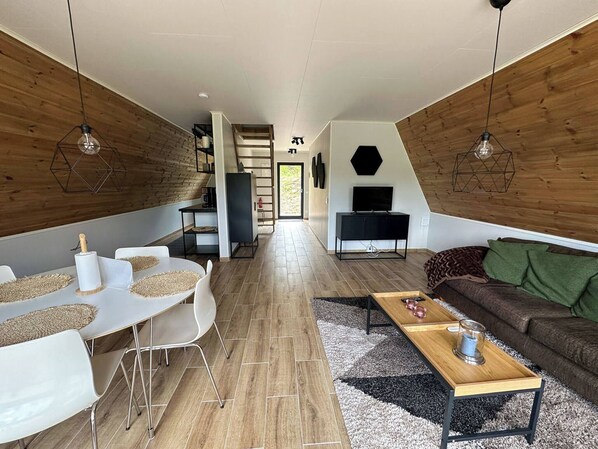 Un espacio habitable moderno con comedor, sofá, televisor y una escalera que sube a un nivel superior.