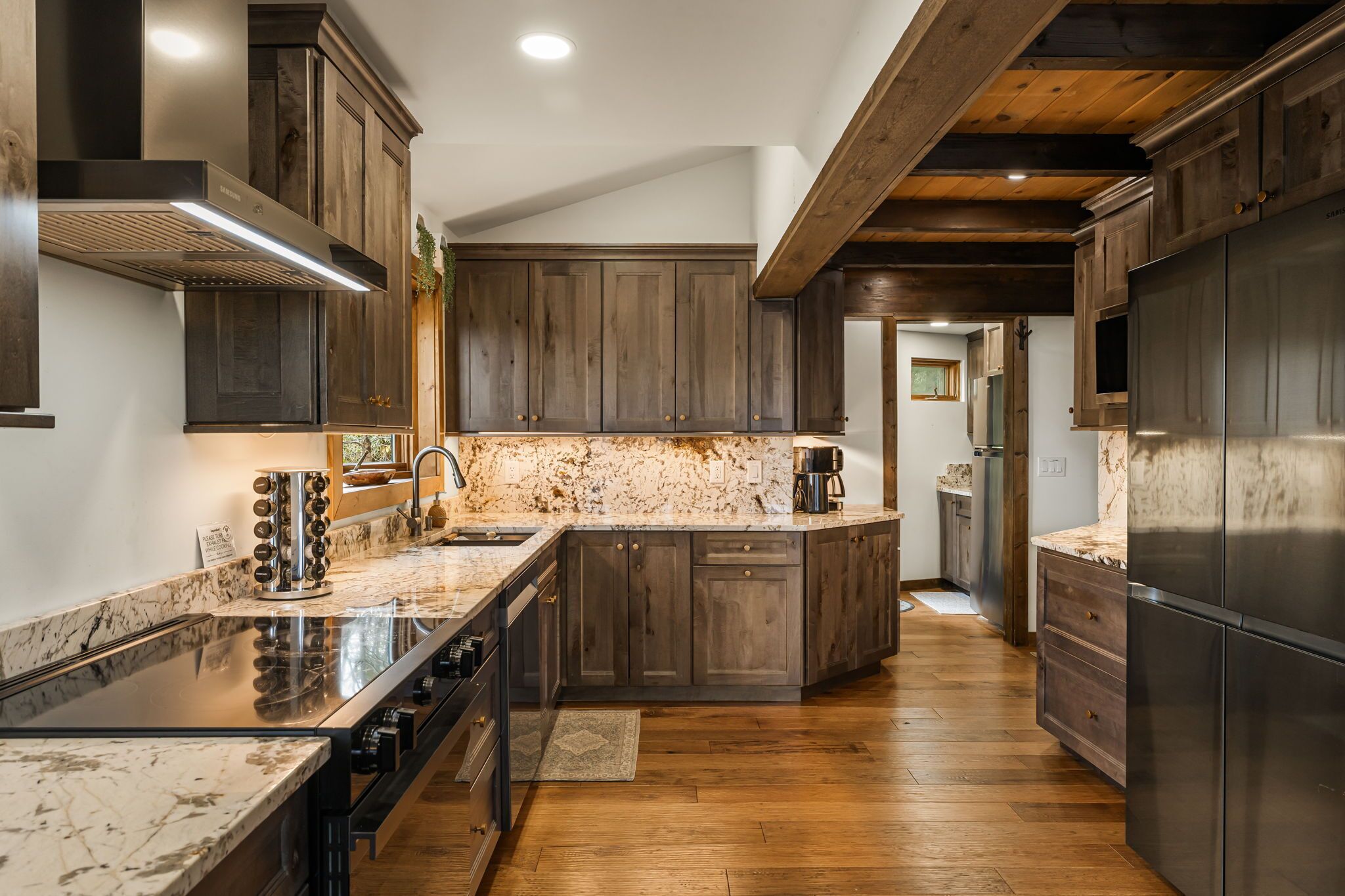 A modern kitchen with dark wood cabinets, a granite countertop, stainless steel appliances, and a wooden ceiling.