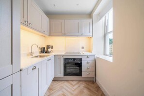 A compact kitchen with white cabinets, a built-in oven, and a window providing natural light. - Beautiful 1-Bed Flat with High Ceilings - VAT Q (Bath)