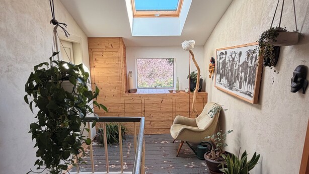 Um quarto estilo loft com claraboia, vigas de madeira, uma cadeira, plantas em vasos e um quadro na parede.