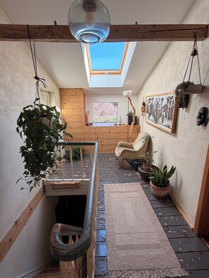 A loft-style room with a skylight, wooden beams, a chair, potted plants, and a framed picture on the wall.