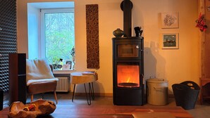 Quarto acolhedor com lareira a lenha, uma cadeira, uma mesa e janela com vista para árvores.