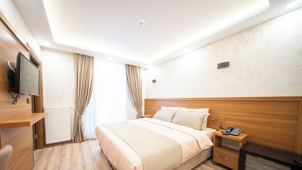 A hotel room with a bed, bedside table, TV, and a built-in heater.