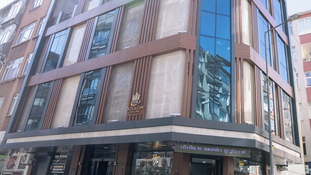 Een meerlaags hotel met een moderne glazen gevel, grote ramen en een opvallend logo op de begane grond.