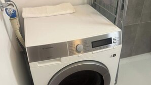 Een voorlader wasmachine met bedieningspaneel, een witte handdoek erboven en een slang aan de zijkant.