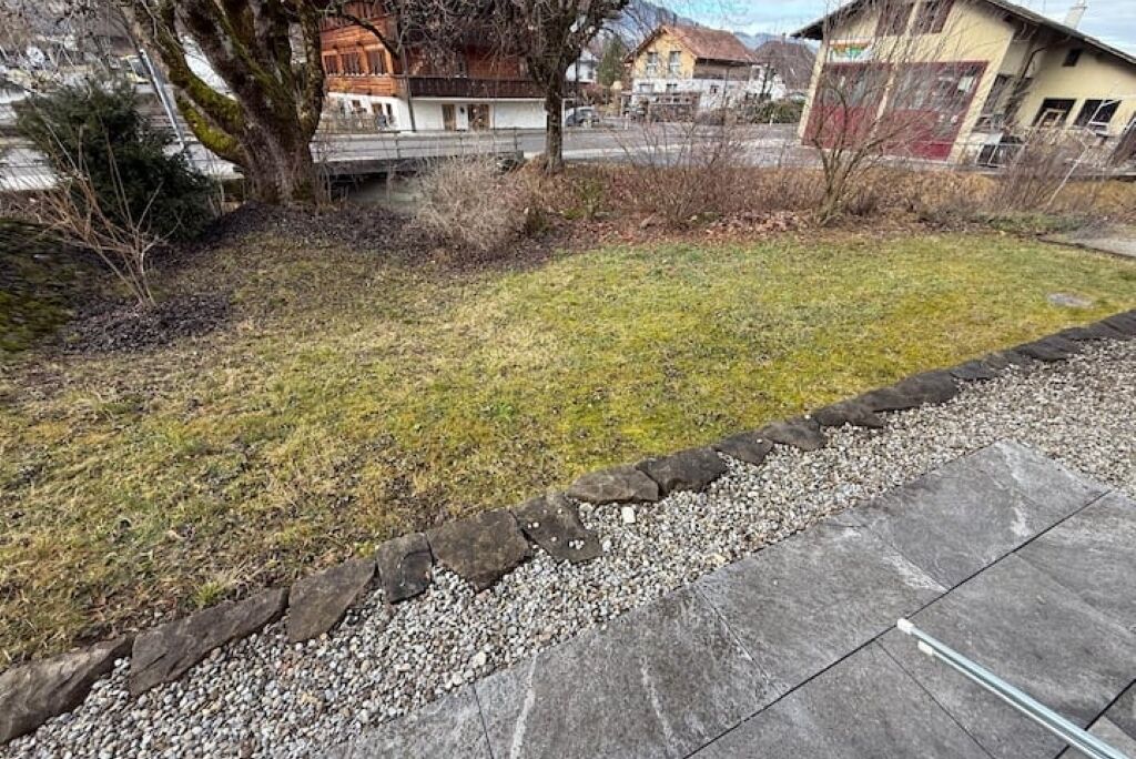 Ein Wohngebiet mit Rasenfläche, einer Steinumrandung und Häusern im Hintergrund.