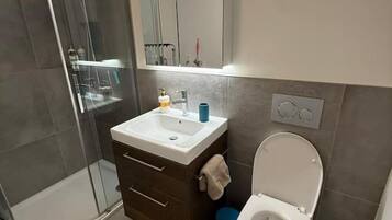 Un baño con cabina de ducha de vidrio, un lavabo con espejo, un inodoro y un perchero para toallas.