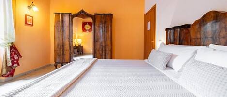 A hotel room with a large bed, wooden headboard, a mirror, and a door leading to another room.