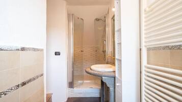 Un baño con ducha de vidrio, lavamanos sobre pedestal y piso de baldosas.