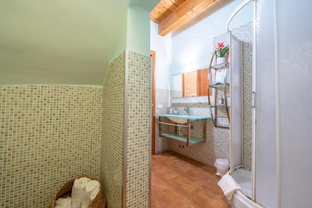A bathroom with mosaic tile walls, a glass shower enclosure, a wooden ceiling, and a visible sink area.