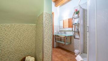 A bathroom with mosaic tile walls, a glass shower enclosure, a wooden ceiling, and a visible sink area.
