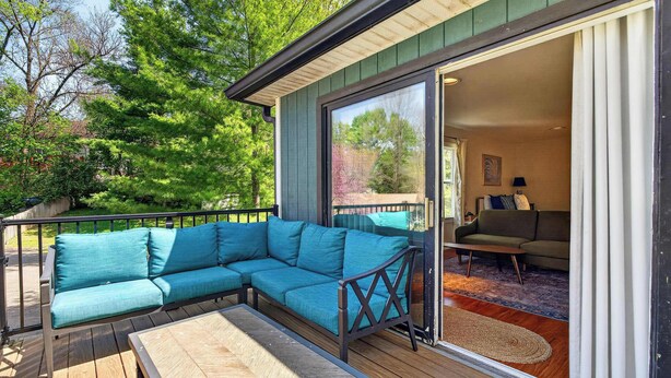 A covered deck with a sectional sofa, a table, and a sliding glass door leading to an interior living area with a couch and a rug. - Relaxing stay near Louisville's top attractions! (Louisville)