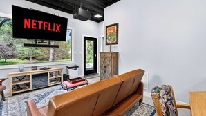 A living room with a large flat-screen TV displaying 'NETFLIX,' a wooden entertainment unit, a brown leather sofa, and a patterned rug. - Relaxing stay near Louisville's top attractions! (Louisville)