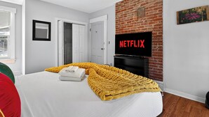 Ein Hotelzimmer mit Bett, einem an einer Backsteinwand befestigten Fernseher und einer Tür zu einem Schrank.