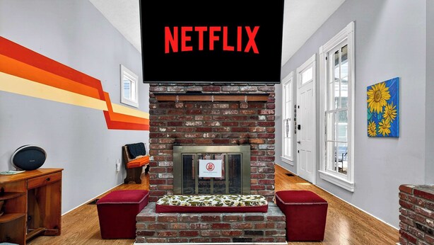 Ein Zimmer mit Kamin, Netflix-Logo, Schreibtisch aus Holz und einer roten Bank.