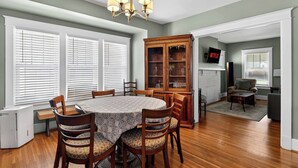 A dining area with a round table, chairs, a chandelier, a wooden cabinet, and a television on a wall. - Spacious home w/ yard near Downtown attractions! (Louisville)