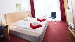 A hotel room with two beds, a desk, a chair, and a small table. - Hotel Haus vom Guten Hirten (Münster)