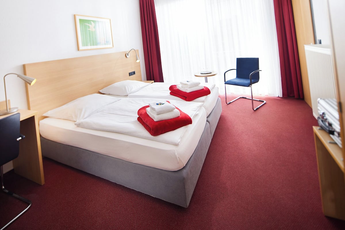Ein Hotelzimmer mit zwei Betten, einem Schreibtisch, einem Stuhl und einem kleinen Tisch.