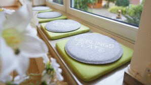 A window seat with cushions labeled 'LIEBLINGS PLATZ' and a view of greenery outside. - Hotel Haus vom Guten Hirten (Münster)