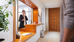 A reception desk with a mirror, a plant, and a wooden door in the background. - Hotel Haus vom Guten Hirten (Münster)