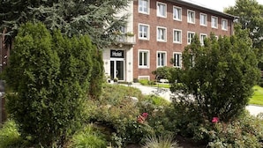 A multi-story hotel with a brick facade, a visible entrance, and a well-maintained garden with various shrubs and flowers. - Hotel Haus vom Guten Hirten (Münster)