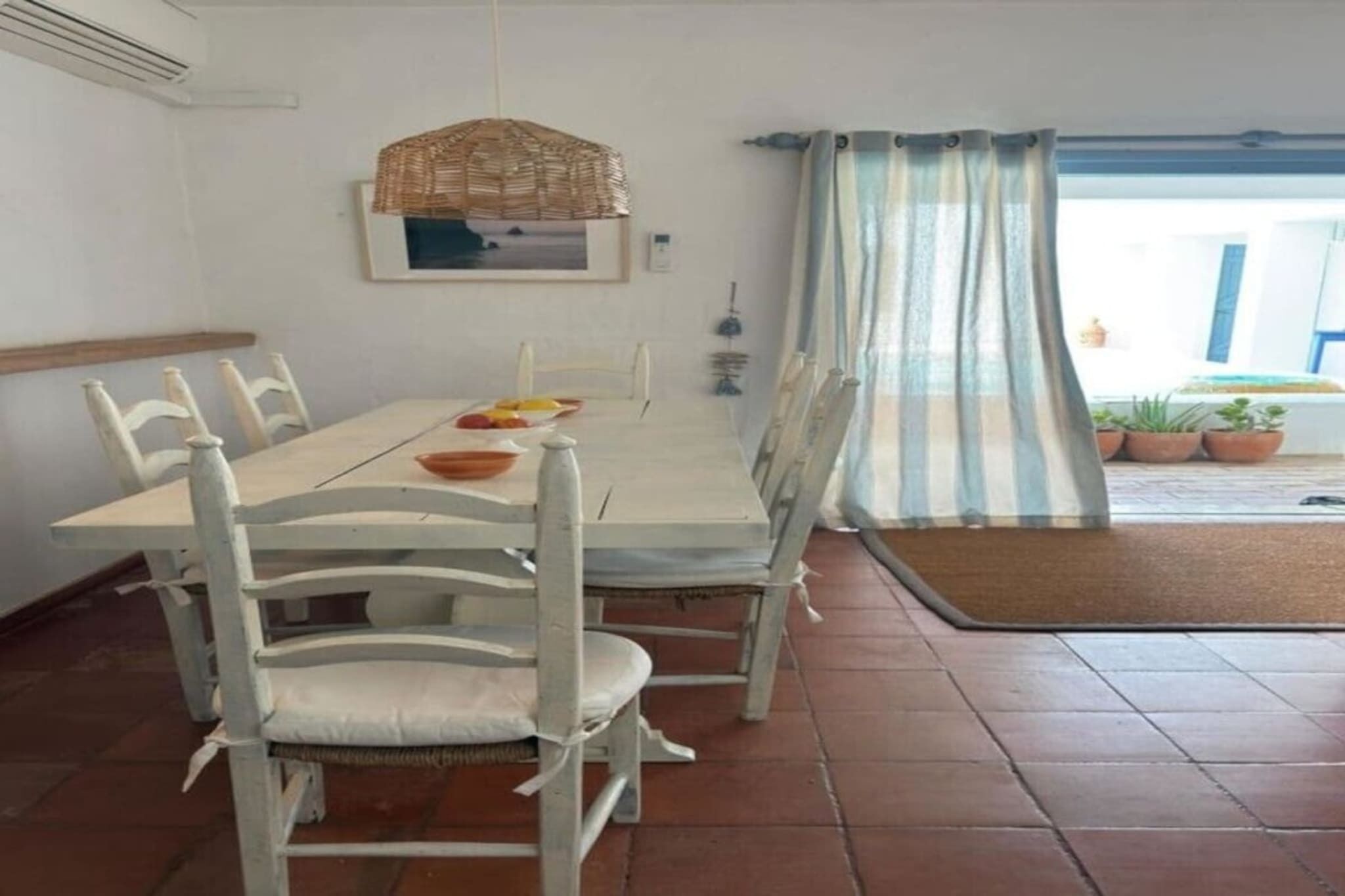 Een eetgedeelte met een tafel, stoelen, een hanglamp, een raam met gordijnen en uitzicht op het buiten.